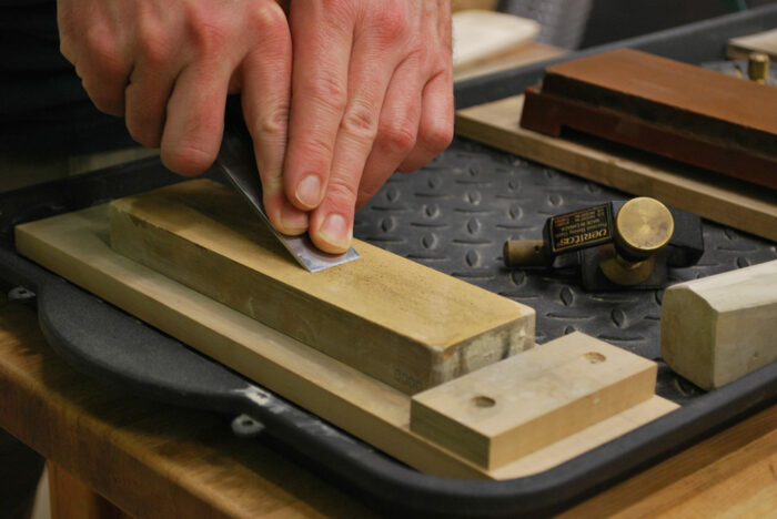A chisel being sharpened on a water stone with a honing guide off to the side.